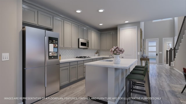 kitchen with light hardwood / wood-style flooring, a kitchen bar, a kitchen island, backsplash, and appliances with stainless steel finishes