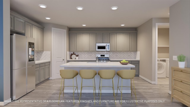 kitchen with washer / clothes dryer, appliances with stainless steel finishes, gray cabinets, and a kitchen island with sink