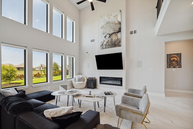 living area with visible vents, baseboards, a ceiling fan, and a glass covered fireplace