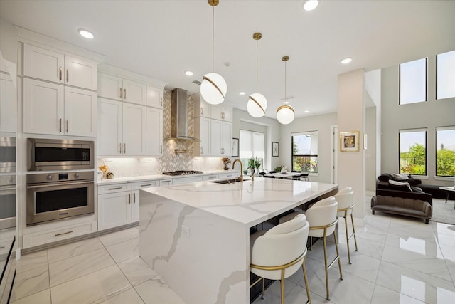 kitchen with a sink, appliances with stainless steel finishes, wall chimney exhaust hood, marble finish floor, and backsplash