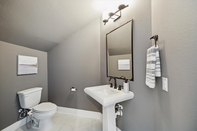 half bath featuring tile patterned flooring, baseboards, toilet, vaulted ceiling, and a textured wall