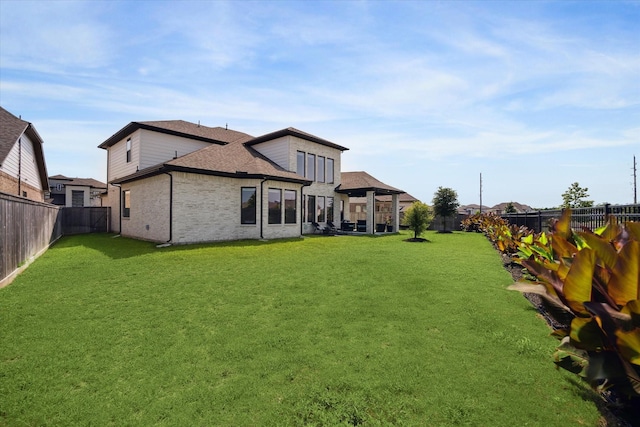 back of house featuring a yard, brick siding, a fenced backyard, and a shingled roof