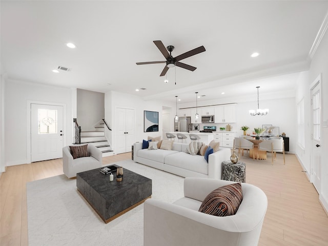 living room featuring ceiling fan with notable chandelier, light wood-type flooring, and crown molding