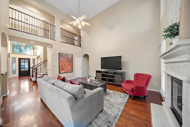 living room featuring ceiling fan, wood-type flooring, a fireplace, and a high ceiling