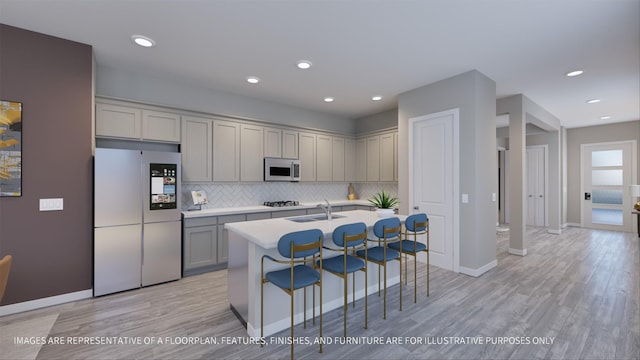 kitchen with sink, fridge, light wood-type flooring, an island with sink, and backsplash