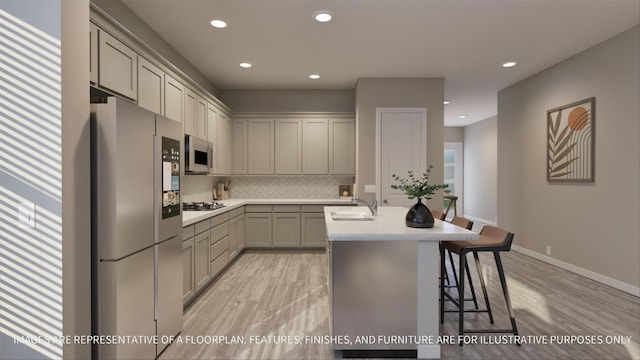 kitchen featuring a center island with sink, backsplash, appliances with stainless steel finishes, a kitchen breakfast bar, and sink