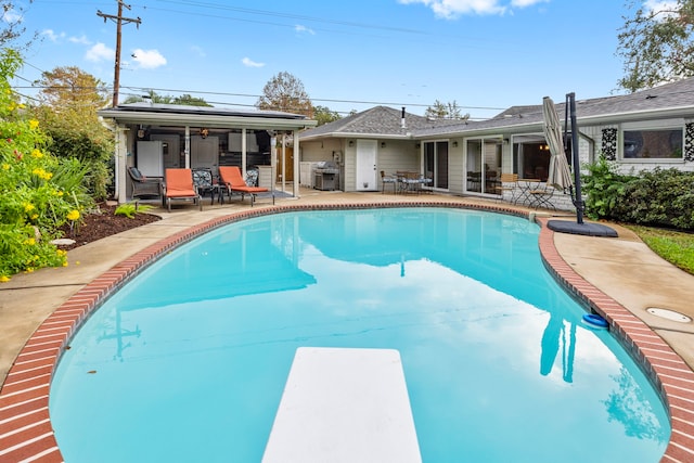 view of pool with area for grilling, a diving board, and a patio area