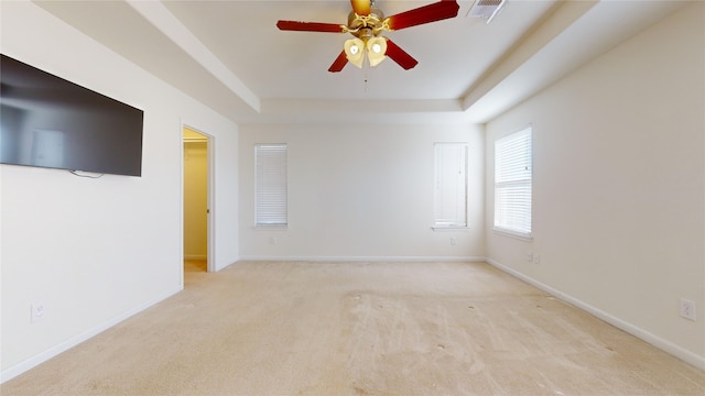 unfurnished room with a raised ceiling, ceiling fan, and light colored carpet