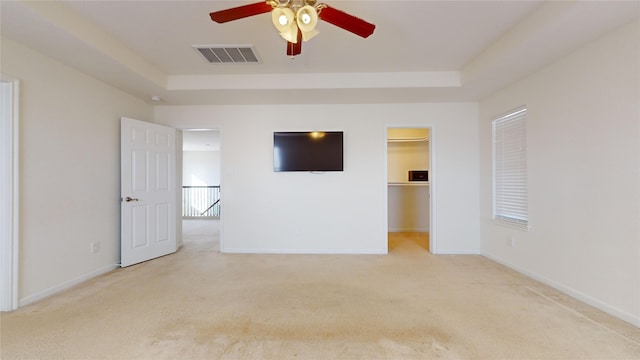 unfurnished bedroom featuring a raised ceiling, a walk in closet, ceiling fan, light colored carpet, and a closet