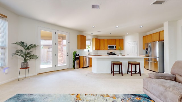 kitchen featuring a kitchen bar, appliances with stainless steel finishes, light colored carpet, a healthy amount of sunlight, and a center island