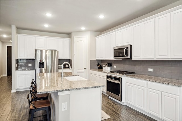 kitchen with appliances with stainless steel finishes, dark hardwood / wood-style flooring, sink, a center island with sink, and white cabinets