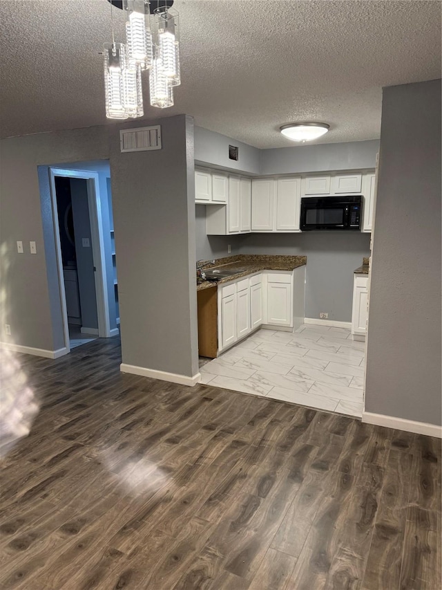 kitchen featuring sink, wood-type flooring, a textured ceiling, hanging light fixtures, and white cabinets