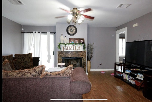 living room featuring ceiling fan, a healthy amount of sunlight, a premium fireplace, and dark wood-type flooring