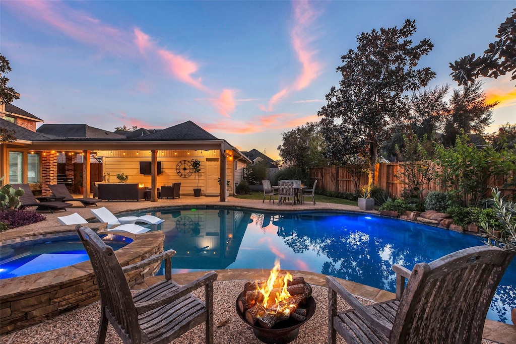 pool at dusk with an outdoor living space with a fire pit, a patio area, and an in ground hot tub