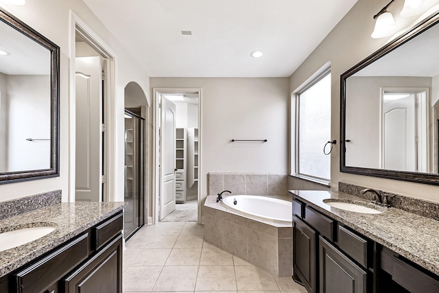 bathroom with tile patterned flooring, vanity, a relaxing tiled tub, and plenty of natural light