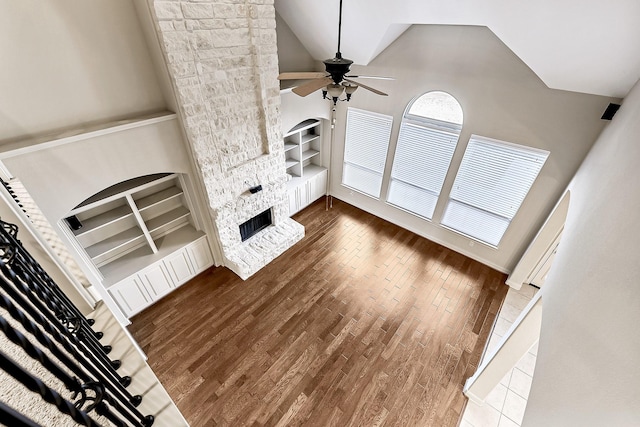 living room with built in shelves, ceiling fan, a stone fireplace, high vaulted ceiling, and hardwood / wood-style floors