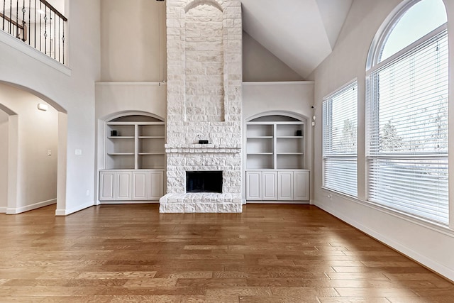 unfurnished living room with built in shelves, a stone fireplace, high vaulted ceiling, and hardwood / wood-style floors