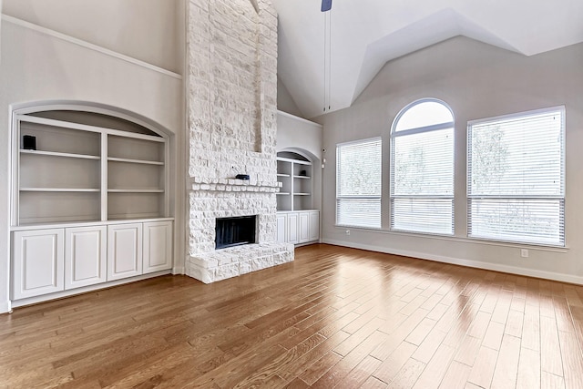 unfurnished living room featuring lofted ceiling, a stone fireplace, built in shelves, ceiling fan, and wood-type flooring