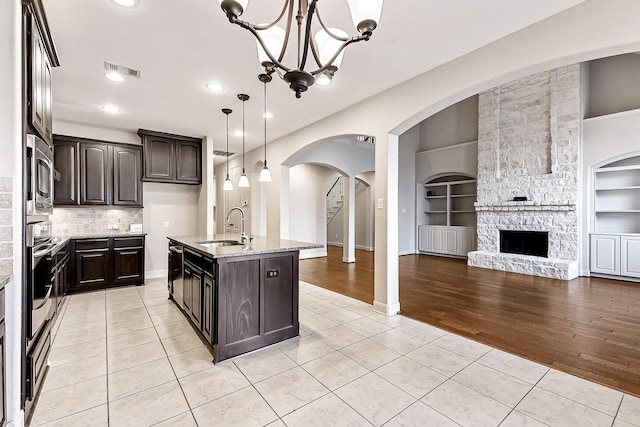 kitchen featuring built in features, light tile patterned flooring, a center island with sink, and sink