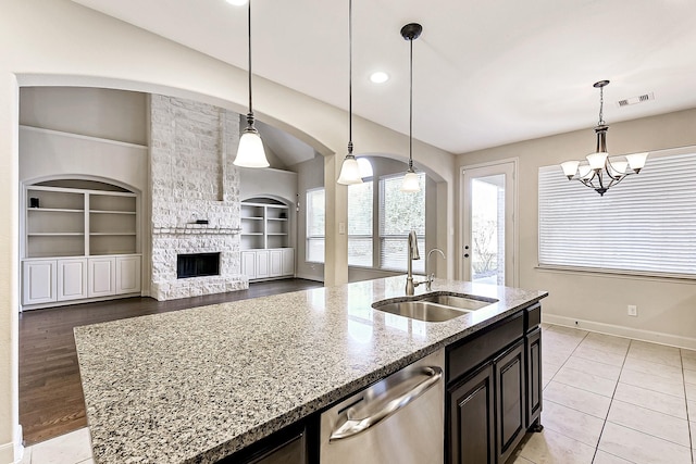 kitchen featuring a kitchen island with sink, hanging light fixtures, sink, stainless steel dishwasher, and built in shelves