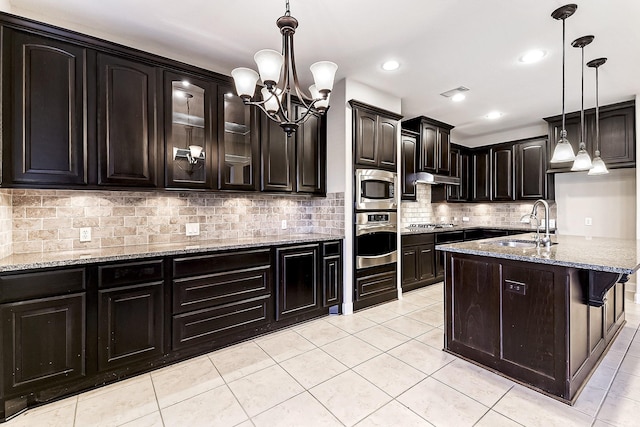 kitchen featuring light stone counters, dark brown cabinetry, stainless steel appliances, sink, and decorative light fixtures