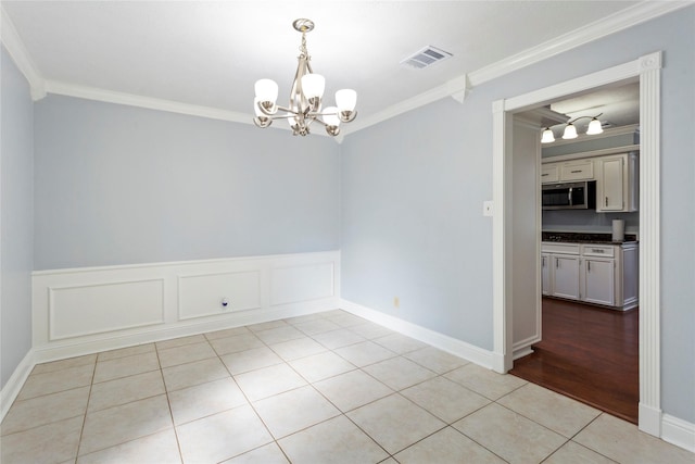 tiled spare room featuring a notable chandelier and ornamental molding