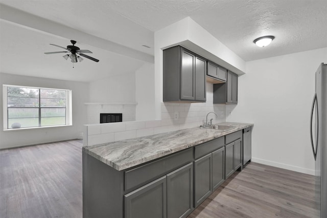 kitchen with gray cabinetry, backsplash, sink, light hardwood / wood-style flooring, and a fireplace