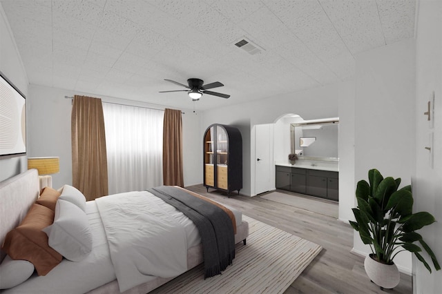 bedroom featuring ceiling fan, ensuite bathroom, and light hardwood / wood-style flooring