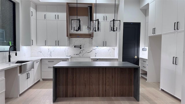 kitchen with light wood finished floors, a kitchen island, decorative backsplash, and a sink