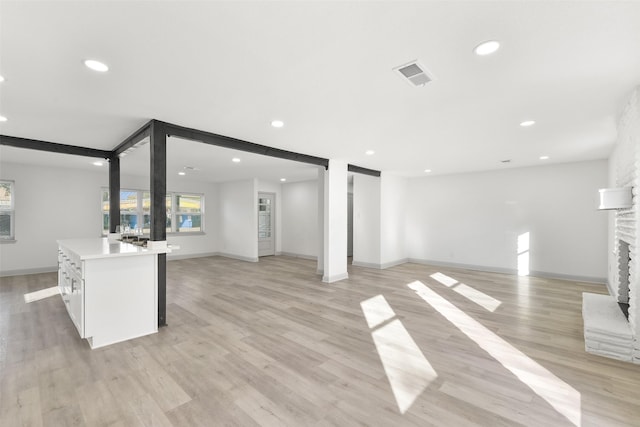 unfurnished living room with a fireplace, light hardwood / wood-style floors, and beamed ceiling