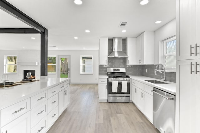 kitchen with white cabinetry, wall chimney range hood, sink, and appliances with stainless steel finishes