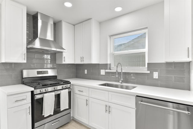 kitchen featuring decorative backsplash, wall chimney exhaust hood, stainless steel appliances, sink, and white cabinetry