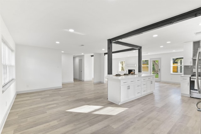 kitchen featuring beam ceiling, stainless steel stove, backsplash, light hardwood / wood-style floors, and white cabinets