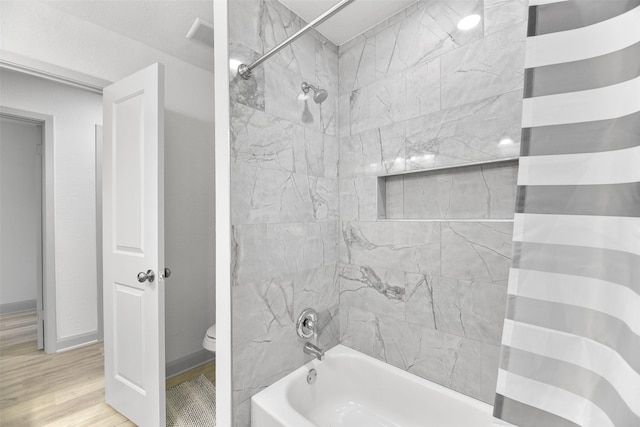 bathroom featuring hardwood / wood-style flooring, toilet, and tiled shower / bath