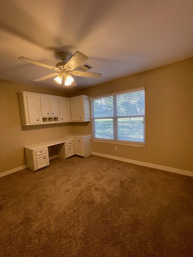 unfurnished office featuring ceiling fan, carpet, and built in desk