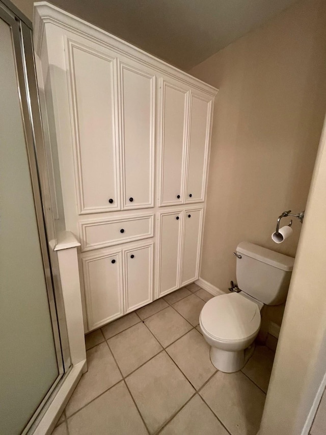 bathroom featuring tile patterned flooring, a shower with door, and toilet