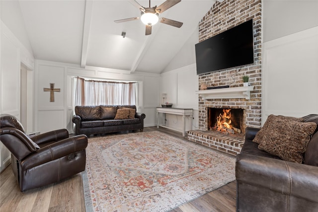 living room with hardwood / wood-style floors, ceiling fan, lofted ceiling with beams, and a brick fireplace