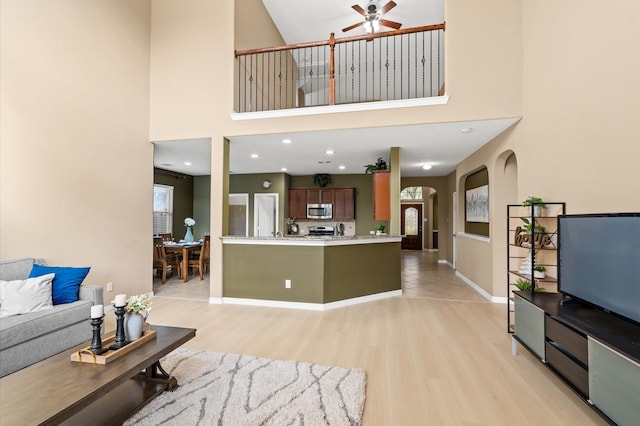 living room featuring a high ceiling, light wood-type flooring, and ceiling fan