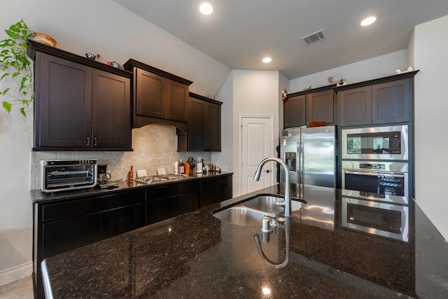 kitchen with dark brown cabinetry, sink, appliances with stainless steel finishes, and dark stone counters