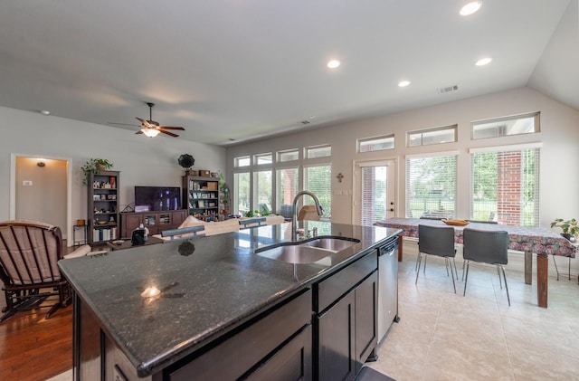 kitchen with ceiling fan, dishwasher, sink, dark stone counters, and a kitchen island with sink