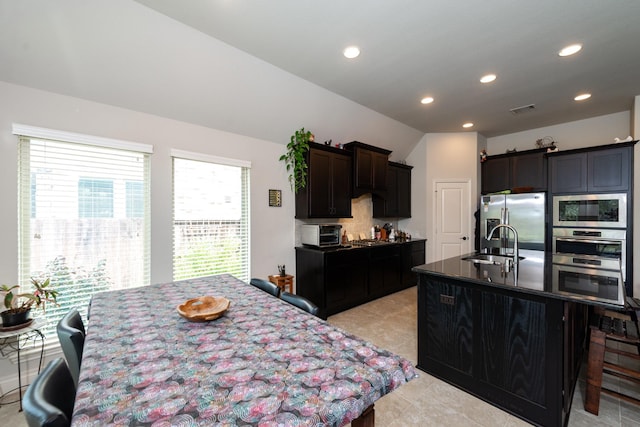 kitchen featuring sink, backsplash, an island with sink, lofted ceiling, and appliances with stainless steel finishes