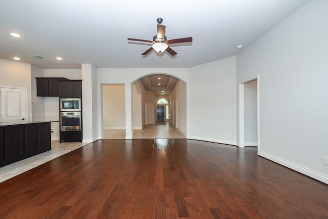 unfurnished living room featuring baseboards, recessed lighting, a ceiling fan, arched walkways, and wood finished floors