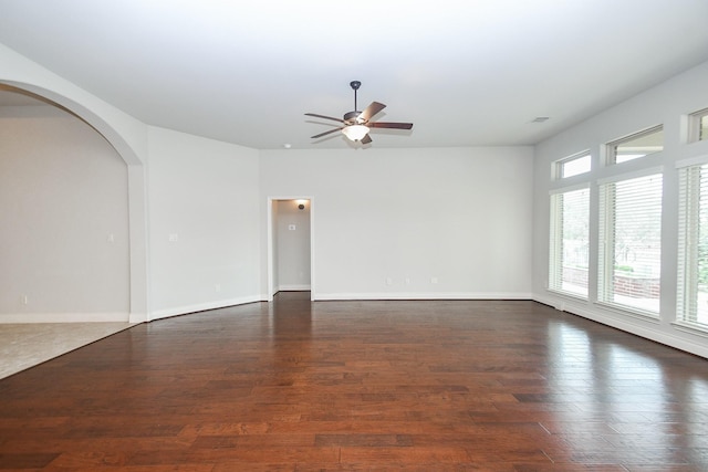 unfurnished living room with baseboards, a ceiling fan, arched walkways, and wood finished floors
