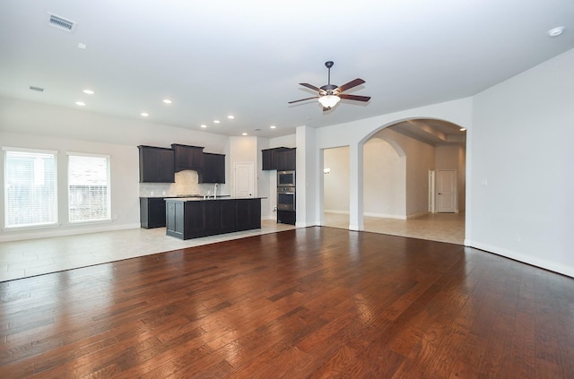 unfurnished living room featuring baseboards, light wood-style flooring, visible vents, ceiling fan, and arched walkways
