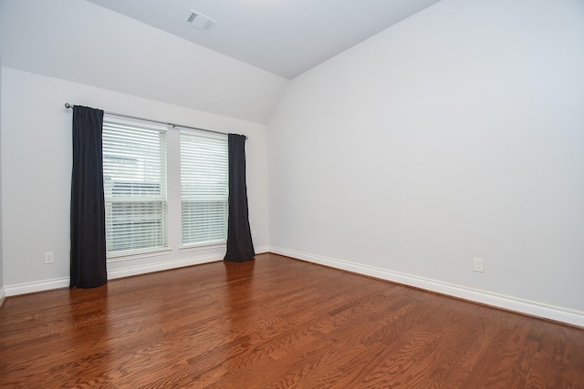 spare room featuring lofted ceiling, visible vents, baseboards, and wood finished floors