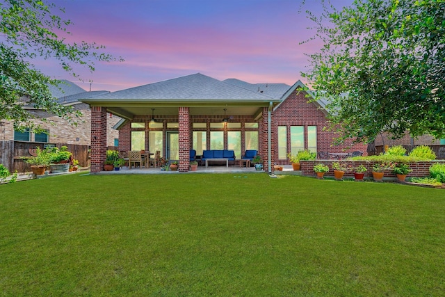 back of property at dusk with brick siding, fence, a patio, and a lawn