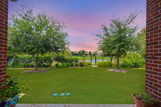 yard at dusk featuring fence and a water view