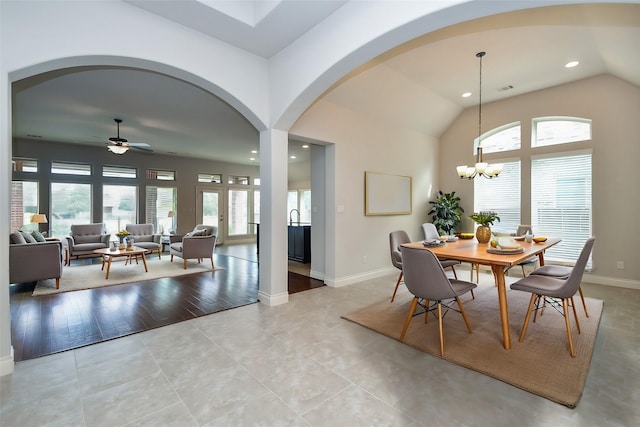 tiled dining room with vaulted ceiling, a healthy amount of sunlight, and ceiling fan with notable chandelier