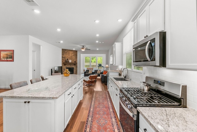 kitchen featuring sink, stainless steel appliances, a stone fireplace, a breakfast bar, and white cabinets