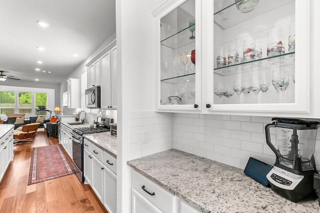 kitchen with backsplash, white cabinetry, stainless steel appliances, and light hardwood / wood-style floors